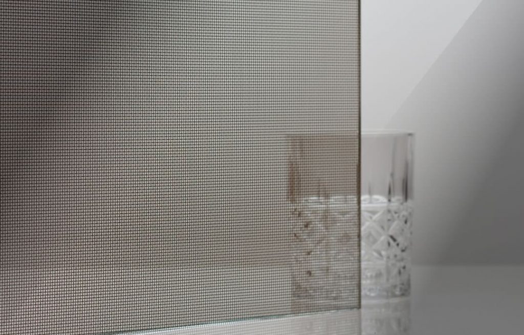 Decorative safety glass created by laminating a woven metal mesh